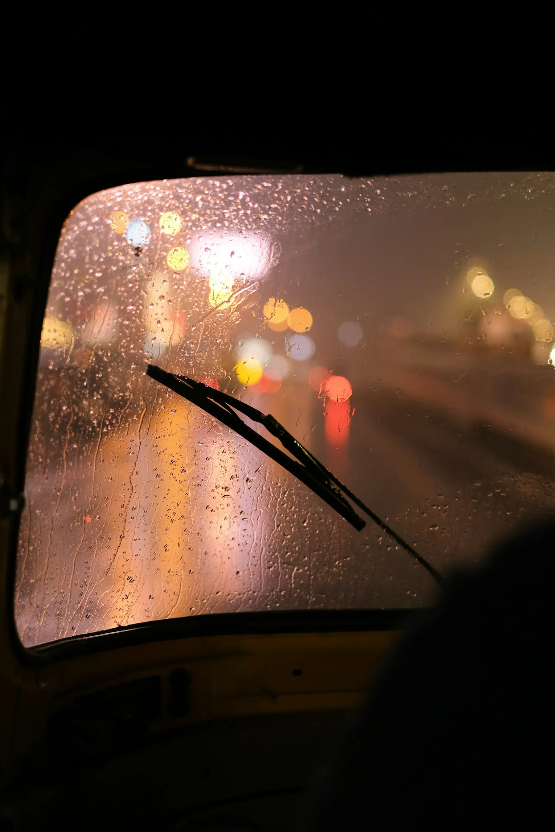 Rain covering a windshield at night with city lights blurred beyond the glass